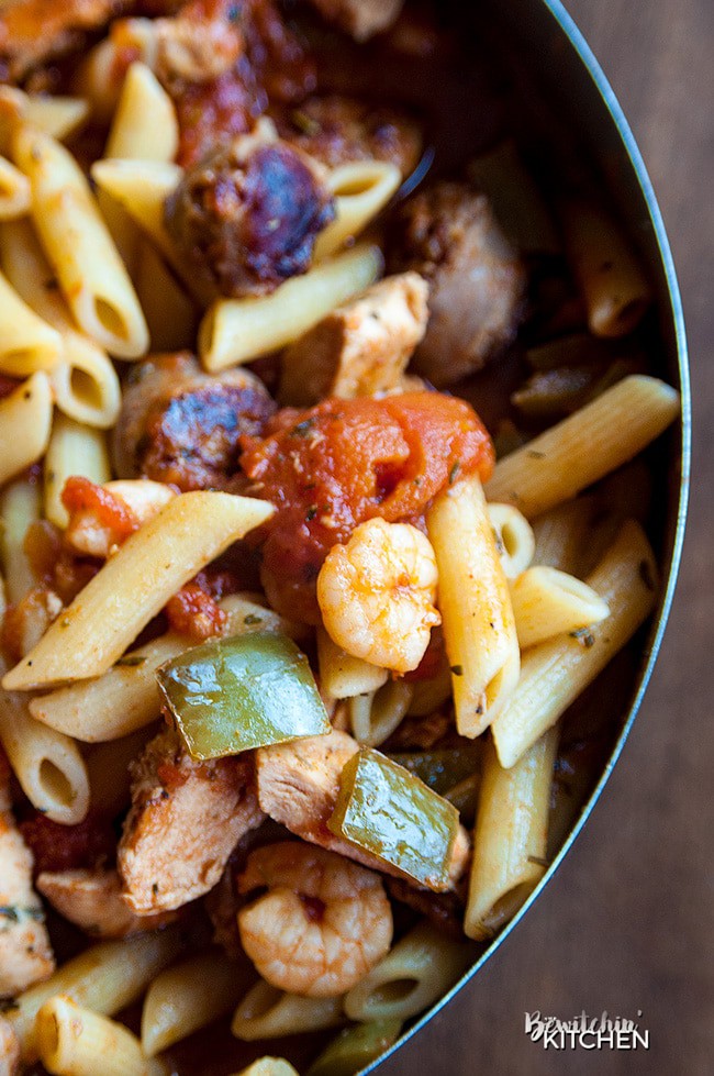 A chef pan full of penne pasta, shrimp, green peppers, tomatoes, and chicken. All the ingredients for Penne Jambalaya!