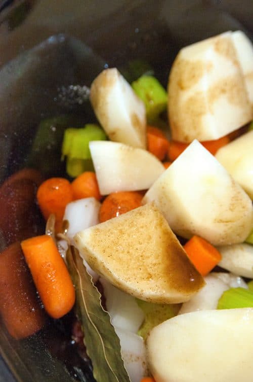 Raw potatoes and vegetables, with a bay leaf, in a slow cooker.