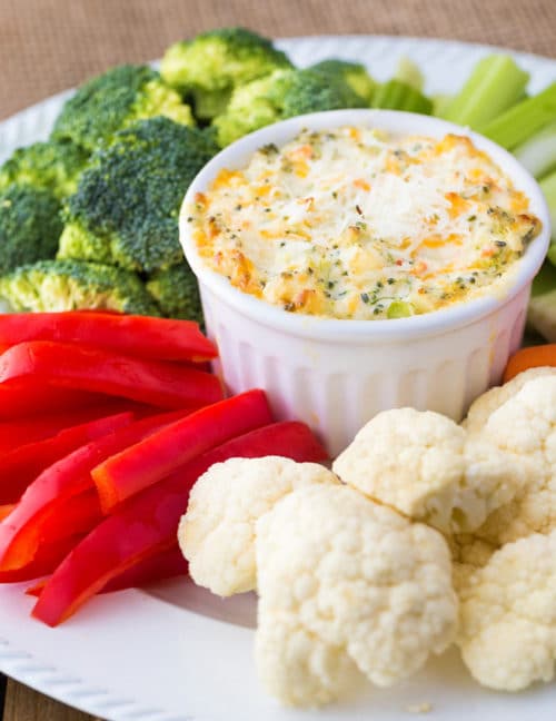 Hot broccoli dip on a serving platter surrounded by broccoli, red pepper, celery, and cauliflower.