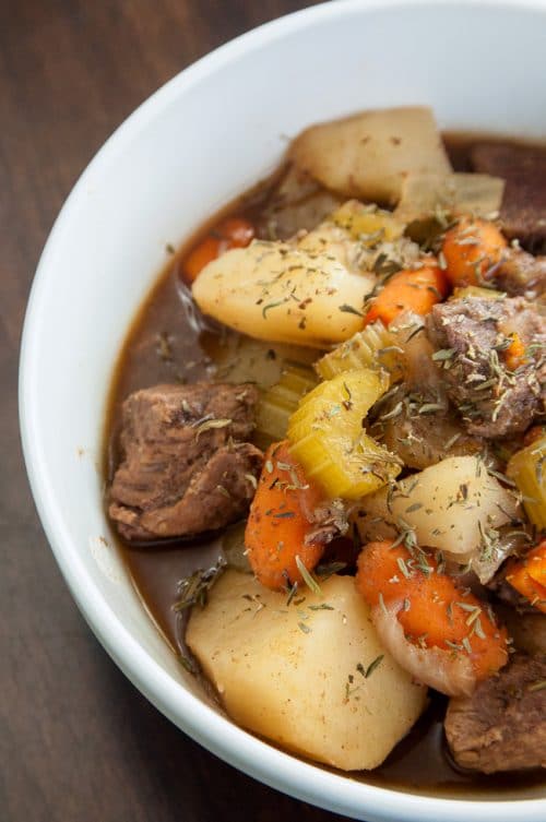 A white bowl full of beef stew with cooked celery, carrots, and potatoes showing.