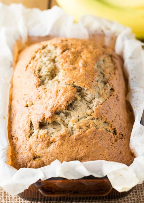 Baked banana bread in a loaf pan lined with parchment paper.