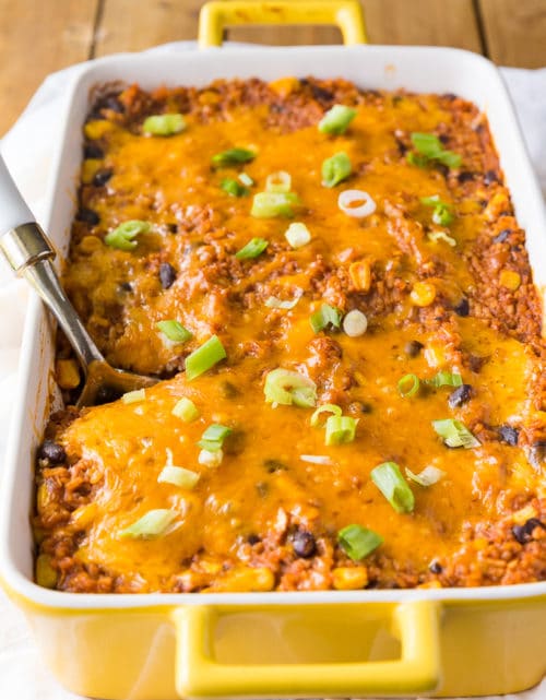 A spoon in a casserole dish filled with cheesy rice filled with mexican flavours and ingredients.