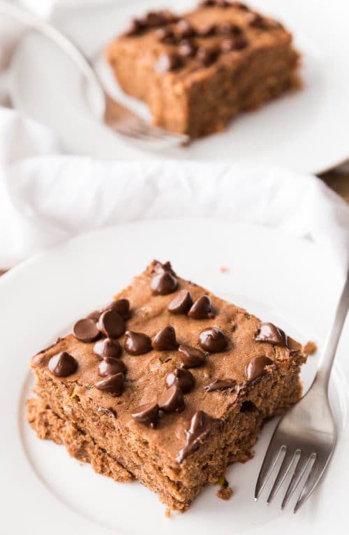 Chocolate Zucchini cake with chocolate chips on top of the cake sitting on a white plate.