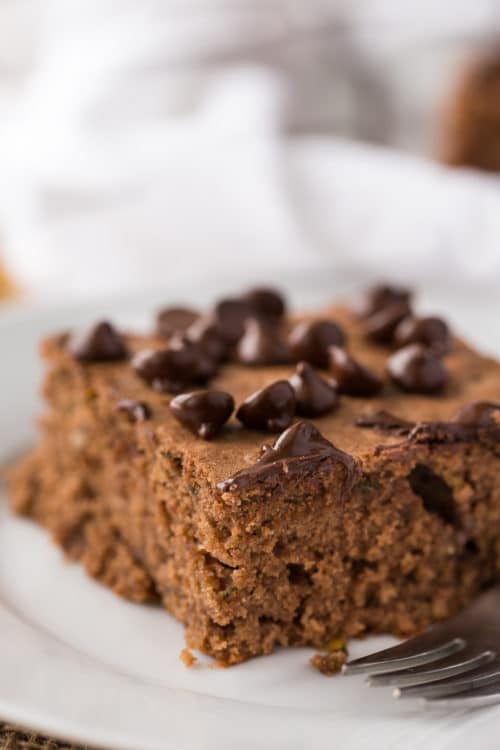 A close up shot of chocolate zucchini cake with chocolate chips sitting on top.