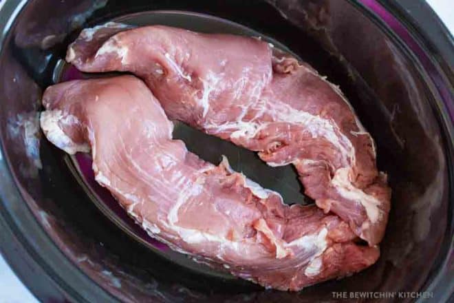 Raw pork tenderloin laying in a slow cooker.