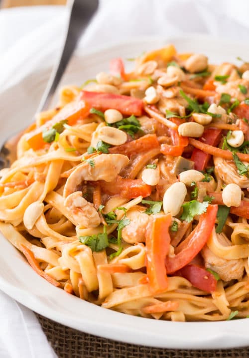 A plate full of fettuccine noodles topped with red peppers, chicken, and peanuts.