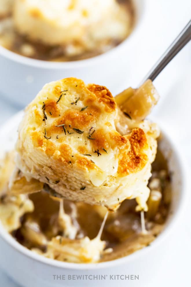 Spoon lifting up french bread smothered in cheese out of a french onion soup bowl.