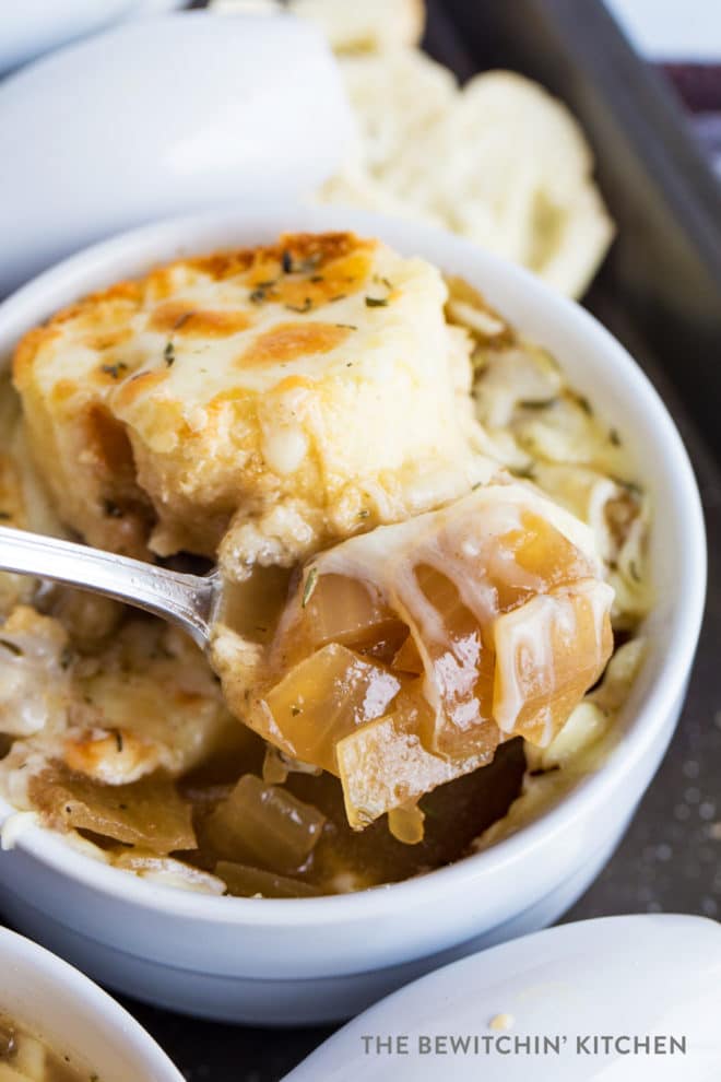 Spoon lifting up onions from a french onion soup bowl.