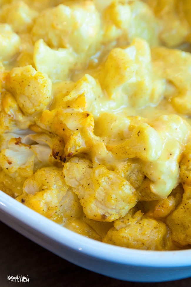 Bubbly curried cauliflower with melted cheddar cheese in a casserole dish.