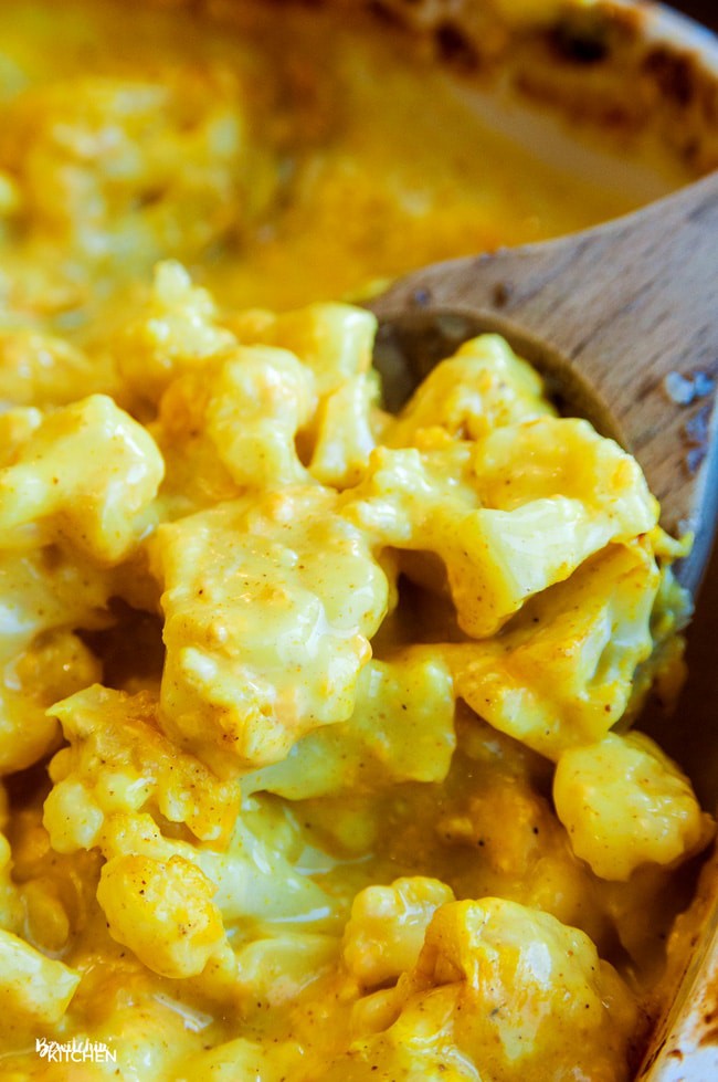 A wooden spoon lifting up the finished side dish of curried cauliflower.