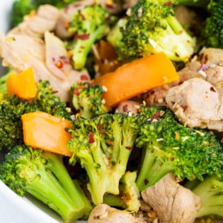 Overhead view of cooked broccoli, orange pepper, red onion, and pork. Stir fried and served on a white plate.