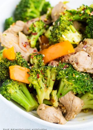 Overhead view of cooked broccoli, orange pepper, red onion, and pork. Stir fried and served on a white plate.
