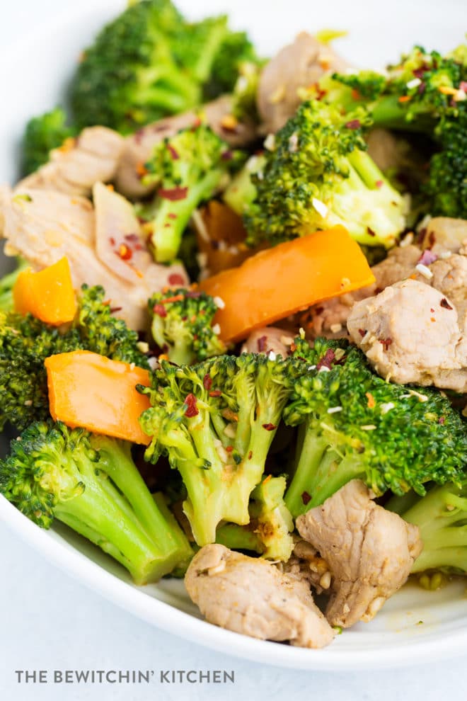 Overhead view of cooked broccoli, orange pepper, red onion, and pork. Stir fried and served on a white plate.