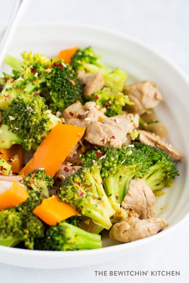 Broccoli, orange bell pepper, and pork tenderloin cooked in a pretty white bowl.