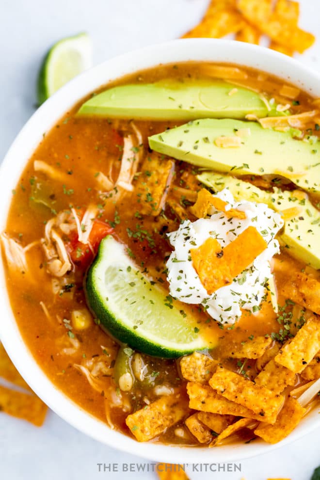 A bowl of chicken tortilla soup with a lime wedge, greek yogurt, avocado. 