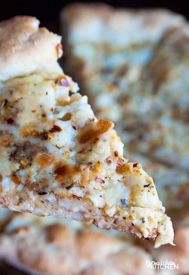 A slice of pizza made with italian salad dressing, parmesan, and cheese lifted towards the camera.