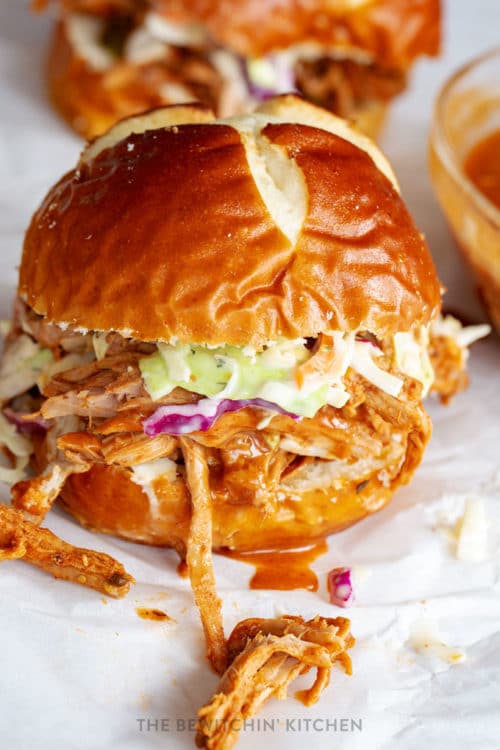 slow cooker pulled pork in a pretzel bun with coleslaw and dripping spicy bbq sauce