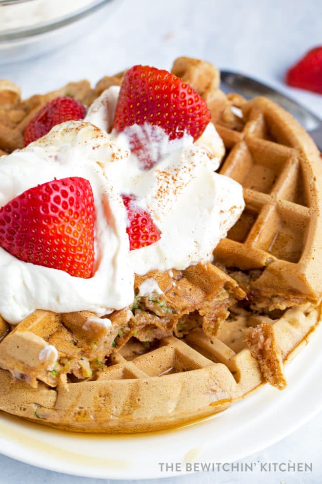 Waffles topped with whipped cream, maple syrup and strawberries cut with zucchini showing.