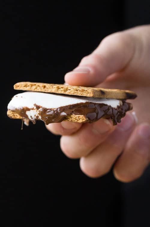 A hand holding bbq s'mores against a black background.