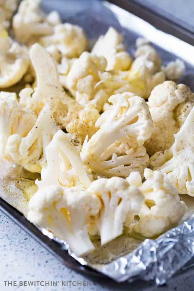 A sheet pan with raw cauliflower sprinkled with garlic powder, salt, and pepper.