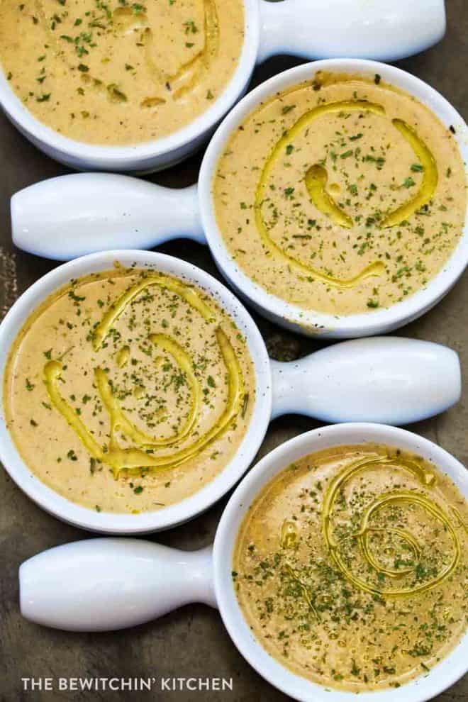 Four bowls full of roasted cauliflower soup topped with parsley and a swirl of olive oil