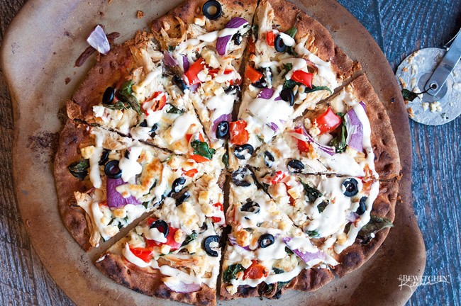 Greek Pizza - pizza crust topped with tangy greek vinaigrette, chicken, red pepper, spinach, olives , purple onion, feta and mozzarella. Finished with a greek tzatziki drizzle. So much yum happening right here. | thebewitchinkitchen.com