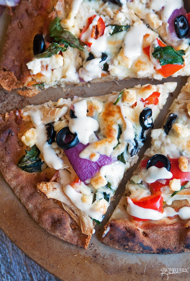 Greek Pizza - pizza crust topped with tangy greek vinaigrette, chicken, red pepper, spinach, olives , purple onion, feta and mozzarella. Finished with a greek tzatziki drizzle. So much yum happening right here. | thebewitchinkitchen.com 