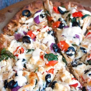 Greek Pizza - pizza crust topped with tangy greek vinaigrette, chicken, red pepper, spinach, olives , purple onion, feta and mozzarella. Finished with a greek tzatziki drizzle. So much yum happening right here. | thebewitchinkitchen.com