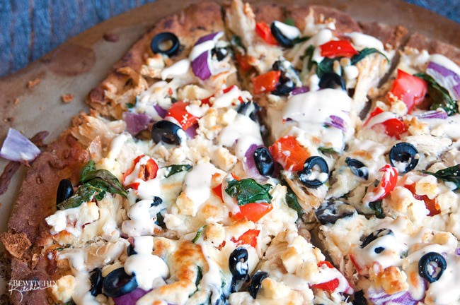 Greek Pizza - pizza crust topped with tangy greek vinaigrette, chicken, red pepper, spinach, olives , purple onion, feta and mozzarella. Finished with a greek tzatziki drizzle. So much yum happening right here. | thebewitchinkitchen.com