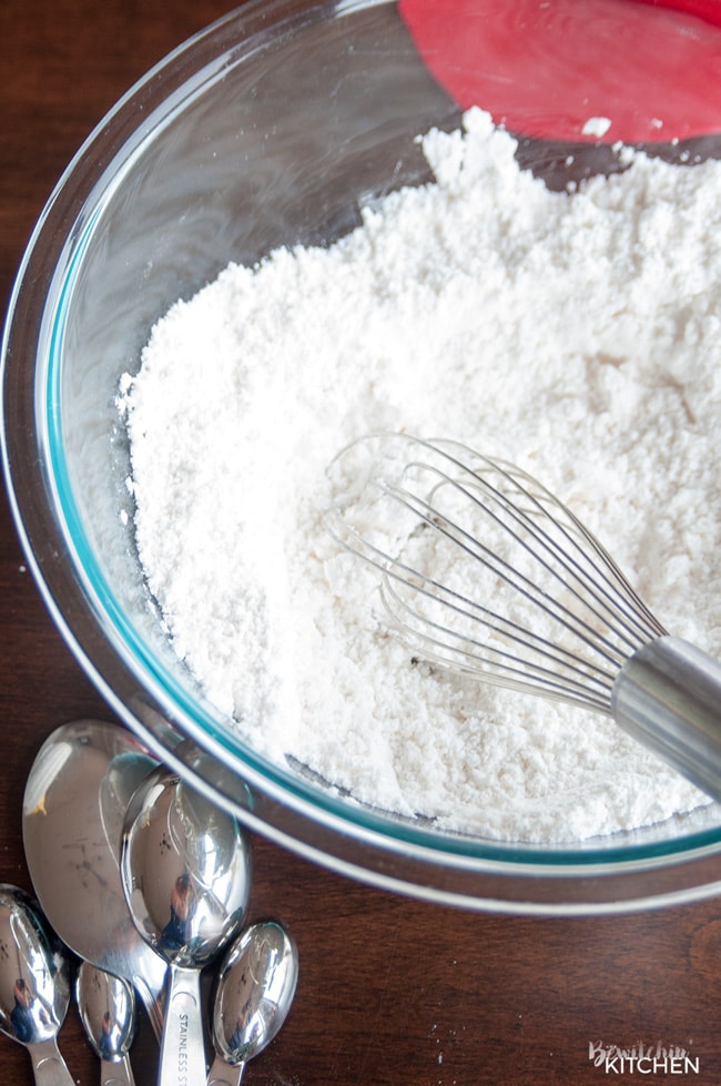 A large glass bowl with gluten free pancake flour and a metal whisk.