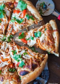 overhead of pizza cutter next to sliced Thai chicken pizza