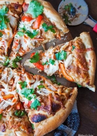 overhead of pizza cutter next to sliced Thai chicken pizza