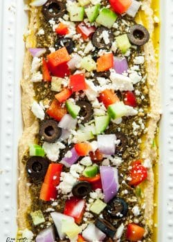 Layered Pesto Greek Dip - EASIEST DIP RECIPE EVER! This Mediterranean inspired appetizer uses hummus, pesto, feta, peppers, olives, and cucumbers. Goes great with veggies and chips. 21 Day Fix approved and a healthy appetizer recipe.