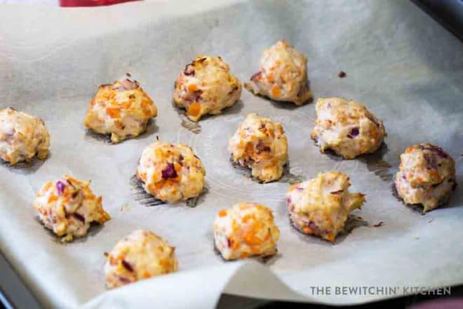 A pan lined with parchment paper, with chicken meatballs stuffed with veggies laying on it.