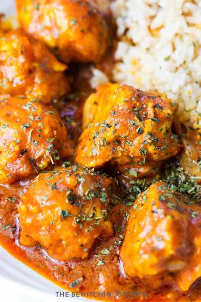 Four chicken meatballs beside a bed of rice with a paleo butter chicken sauce poured over.