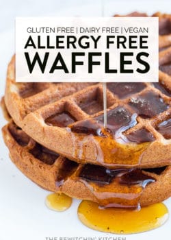 Maple syrup being poured over a stack of fluffy waffles.