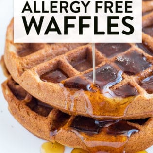 Maple syrup being poured over a stack of fluffy waffles.