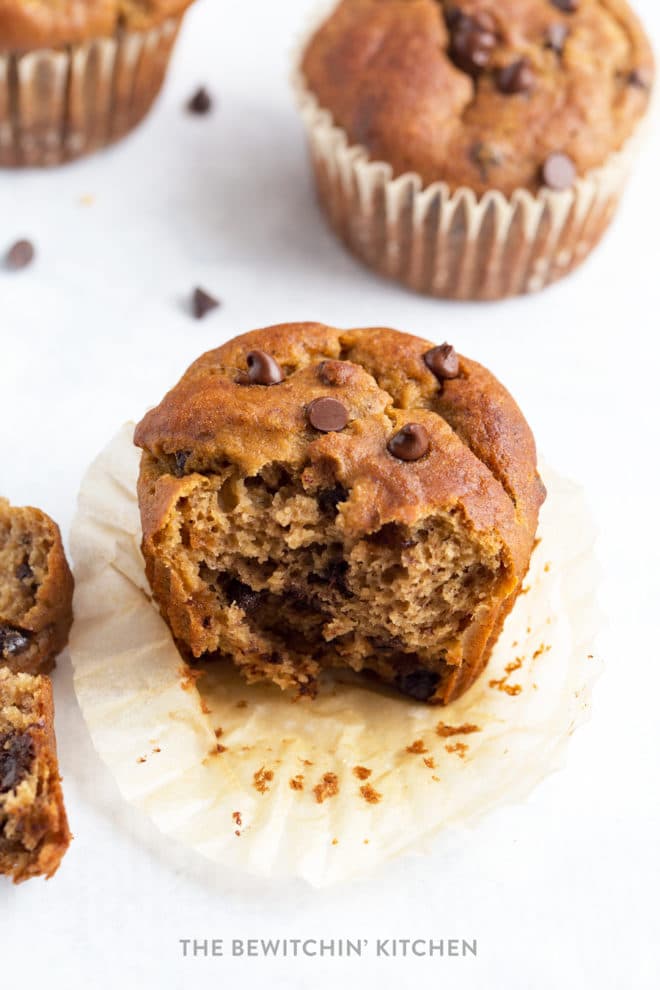 A half eaten gluten free chocolate chip muffin on parchment paper.