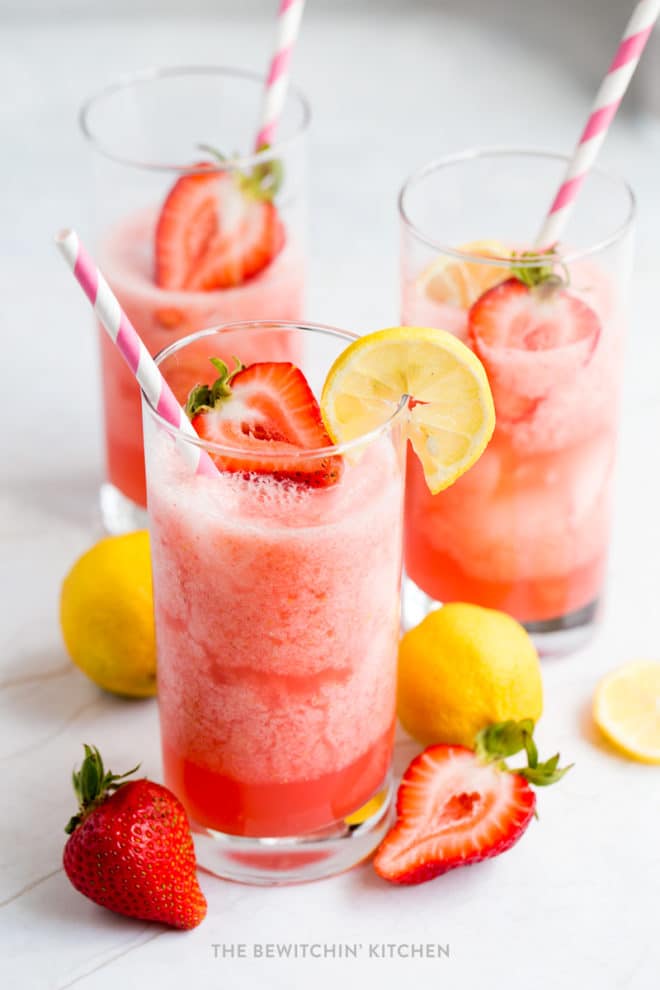 Strawberry lemonade poured in a tall glass with strawberries on top and a pink straw.