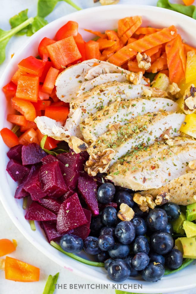 Sliced chicken breast over spinach, beets, carrots, bell peppers, avocado, and blueberries.