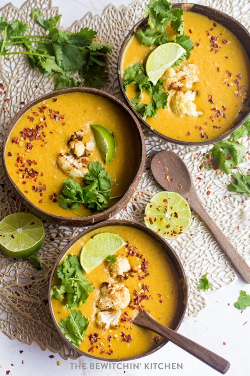 Overlooking three bowls of curried cauliflower soup with limes, chili peppers and cilantro.