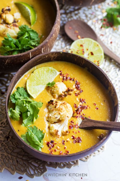 A coconut bowl with curry cauliflower soup in side