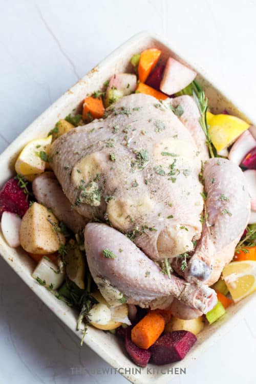 Whole chicken laid over a beets, lemons, carrots, potatoes, celery, and onion.