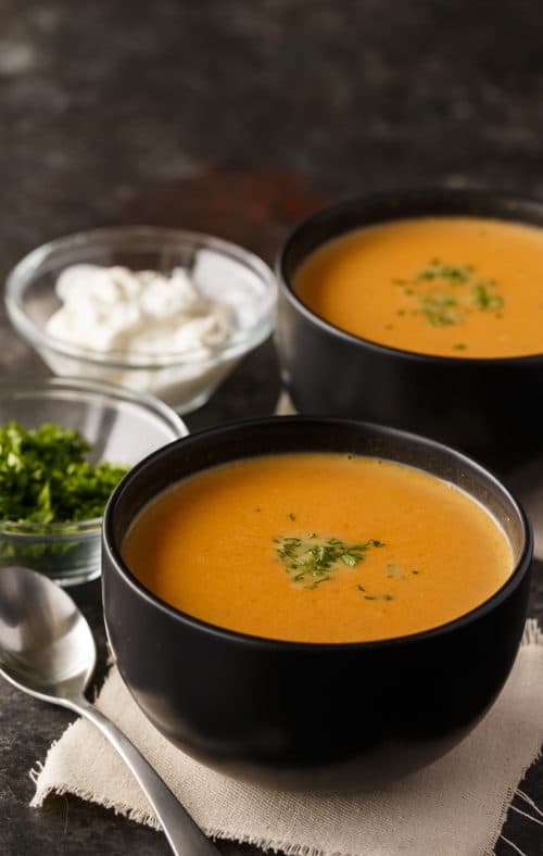 two bowls of pumpkin soup next to sour cream and fresh parsley