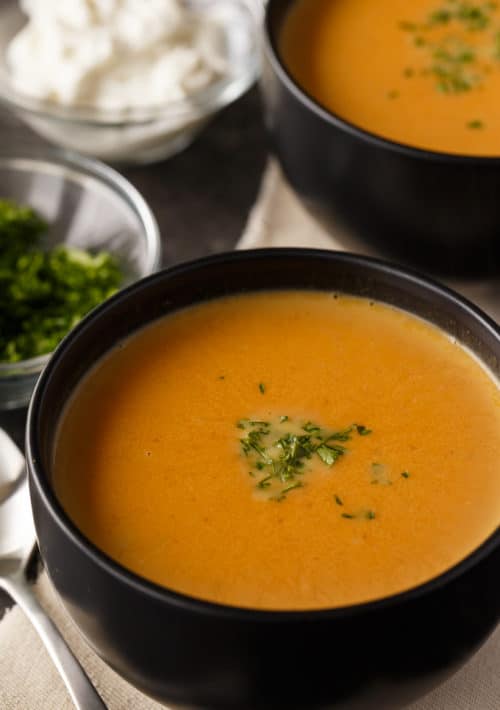 closeup of creamy pumpkin soup surrounded by a second serving and bowls of garnish