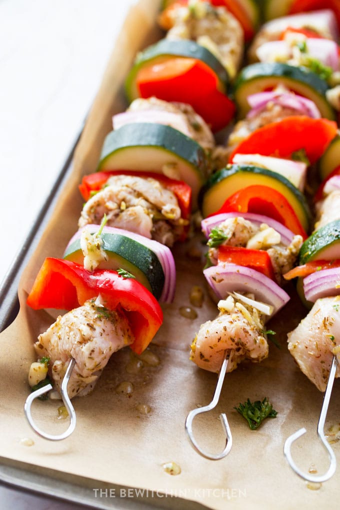 Raw chicken, red pepper, purple onion, and zucchini skewered onto a kebab in a greek marinade.