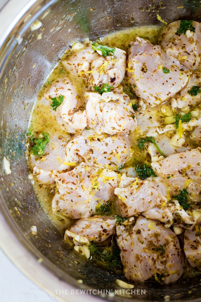 A bowl with chicken souvlaki marinade and raw chicken, cut into chunks.