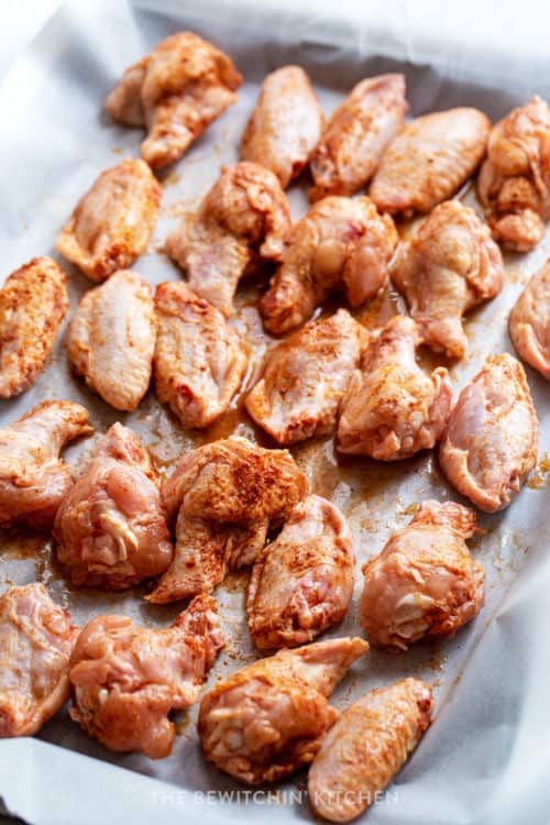 raw chicken wings on a baking sheet lined with parchment paper with chili powder on them