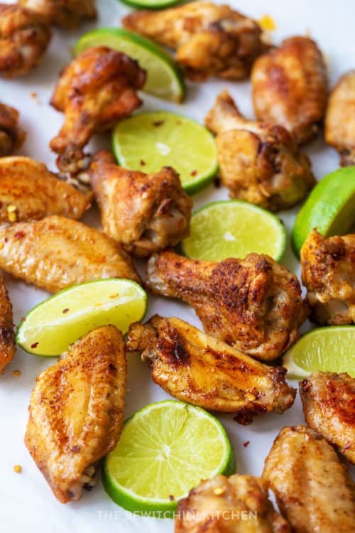 sliced limes and oven baked chicken wings on parchment paper