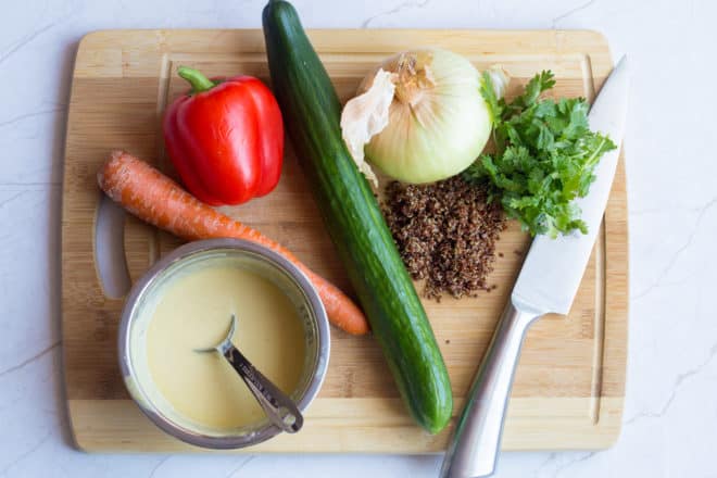 healthy dinner ingredients: cucumber, red peppers, tahini dressing, carrots, onion, quinoa